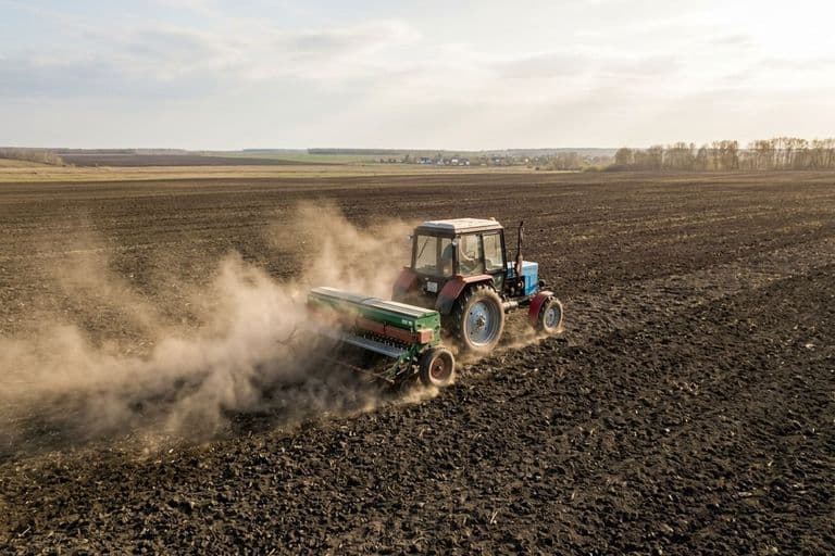 Посев ярового рапса — трактор с сеялкой на поле весной